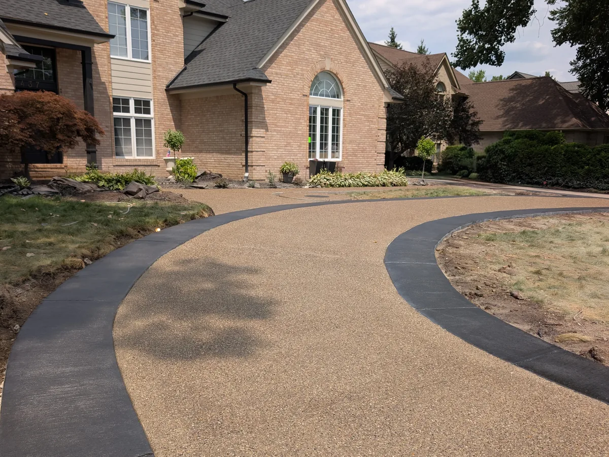 Curved exposed aggregate driveway with charcoal stamped border at a brick home in Troy, MI