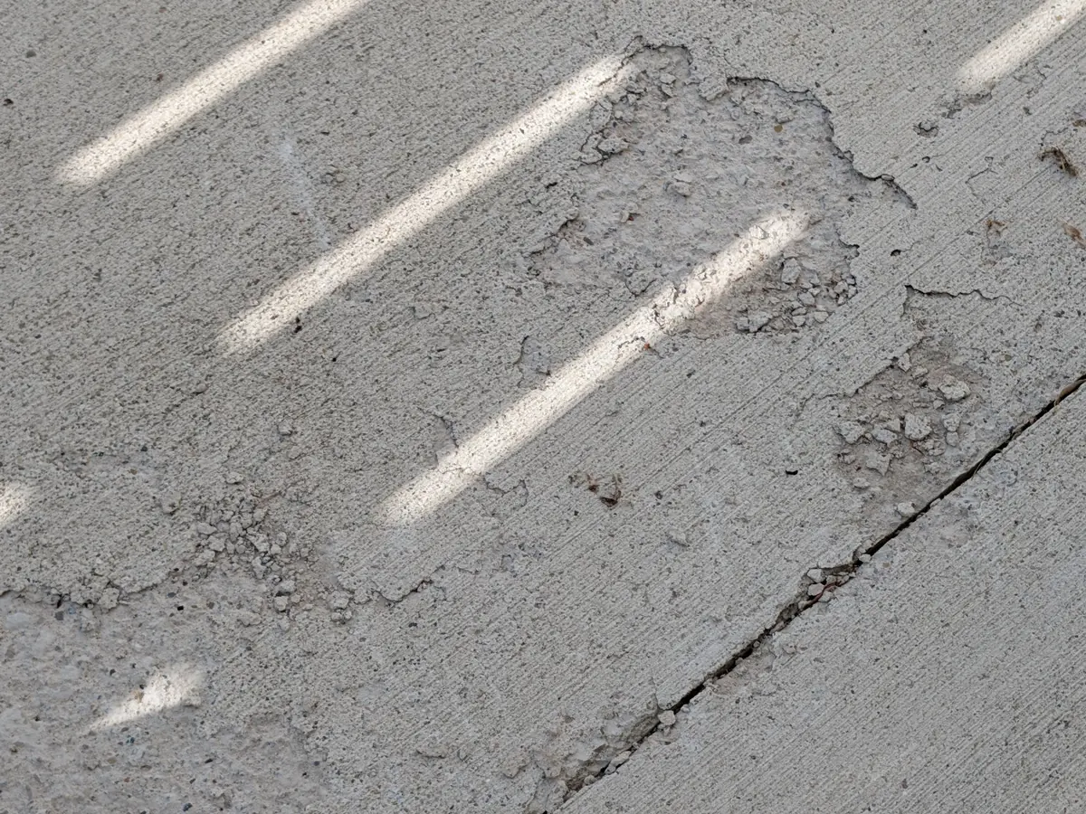 Early-stage concrete spalling and surface scaling on a Metro Detroit driveway, with deterioration along the control joint